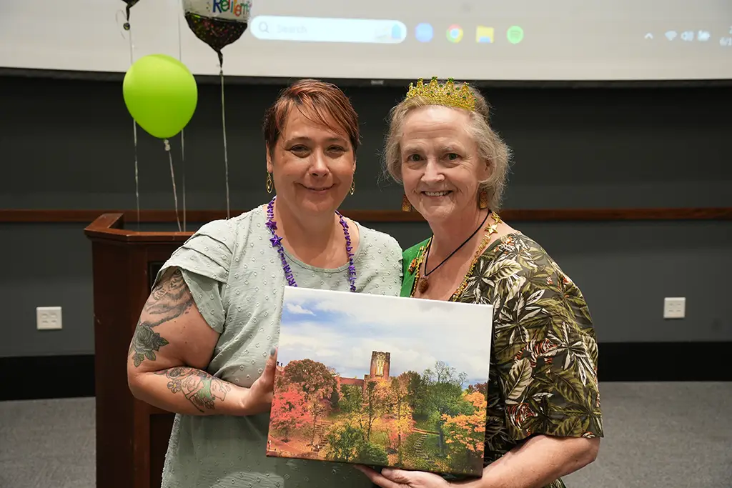 Two women pose together for a photo with a painting of Ayres Hall