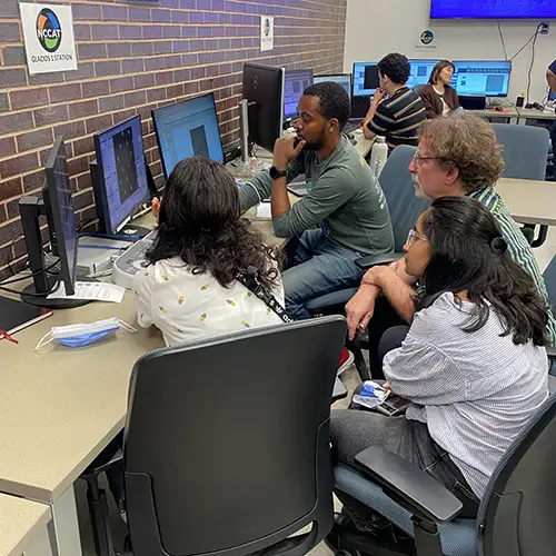 A group of researchers gathered around a set of computer monitors